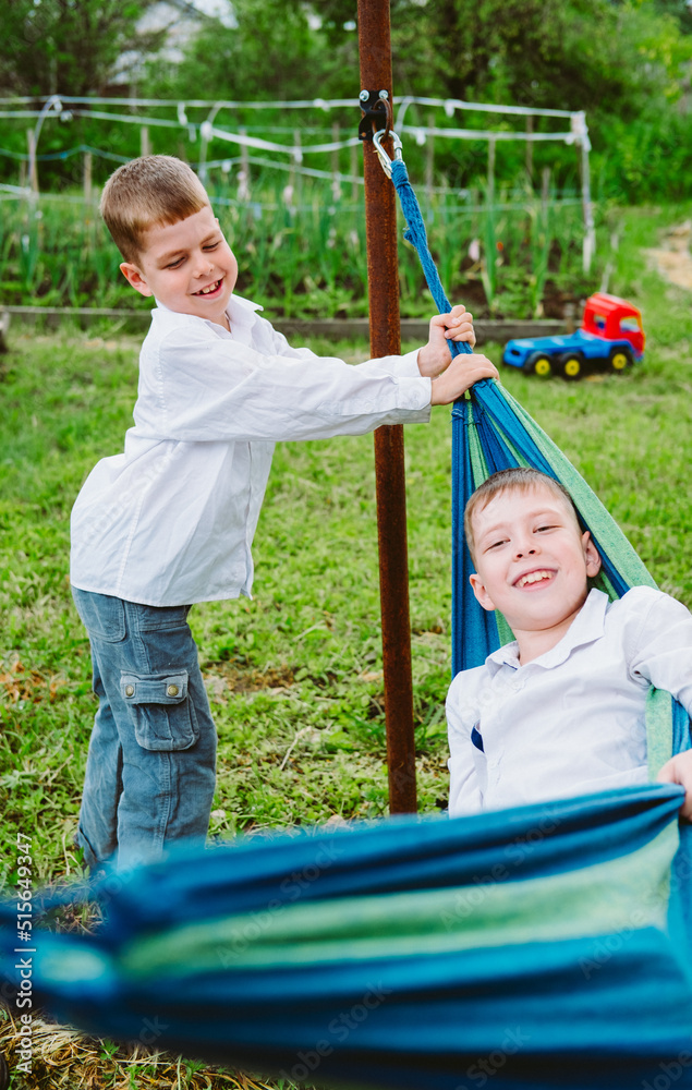 happy children play and ride on a hammock. The kids have fun rolling in a hammock. Summer holidays in the village happy children play and ride on a hammock. The kids have fun rolling in a hammock. Summer holidays in the village