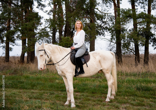 smiling blonde beautiful woman riding  white blue eyed  horse horse in green forest  © Tetatet