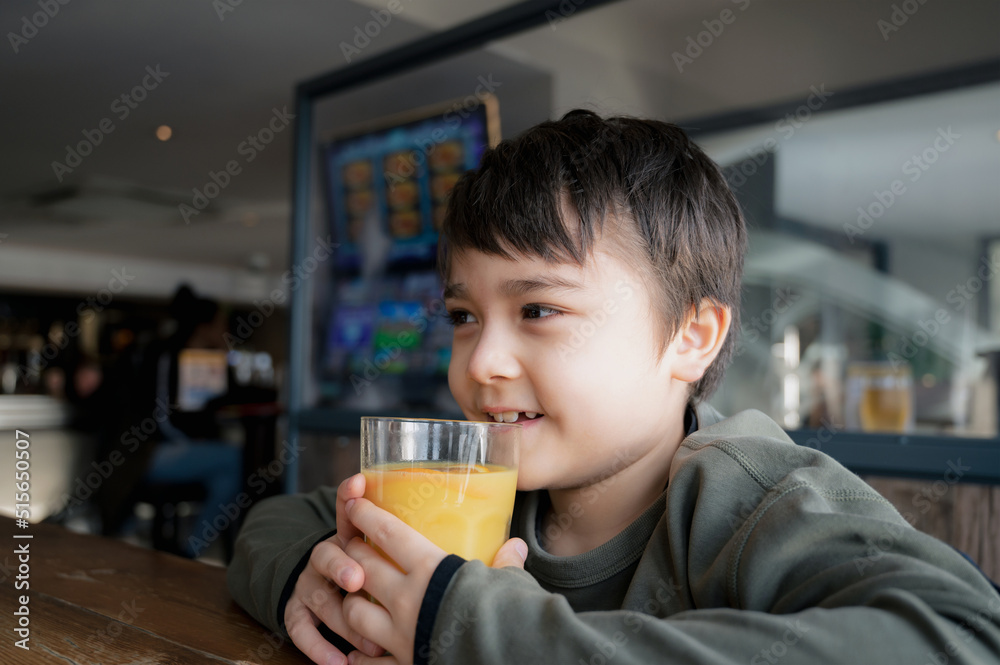 Side view Portrait Young kid drinking fresh orange juice for breakfast in cafe, Happy child boy drinking glass of fruit juice while waiting for food in restaurant, Healthy food lifestyle concept Side view Portrait Young kid drinking fresh orange juice for breakfast in cafe, Happy child boy drinking glass of fruit juice while waiting for food in restaurant, Healthy food lifestyle concept