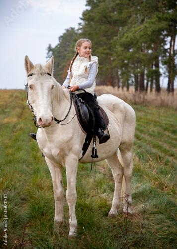 Cute girl sitting on a white blue eyed horse in the autumn forest  © Tetatet