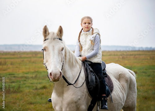Cute girl sitting on a white blue eyed horse in the green field