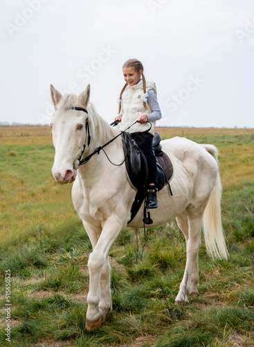 Cute girl sitting on a white blue eyed horse in the green field © Tetatet