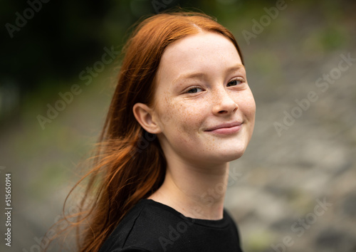 Red haired twelve year old girl with freckles posing with a nature bokeh background
