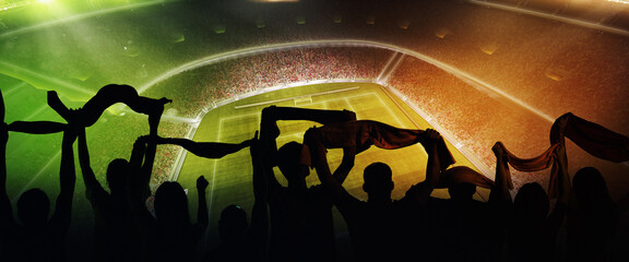 Back view of football, soccer fans cheering their team with scarfs at crowded stadium at evening time. Concept of sport, support, competition. Out of focus effect