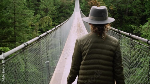 Female traveler wearing a hat, walking along suspension bridge in lush rainforest setting in North Vancouver, British Columbia, Canada.  photo