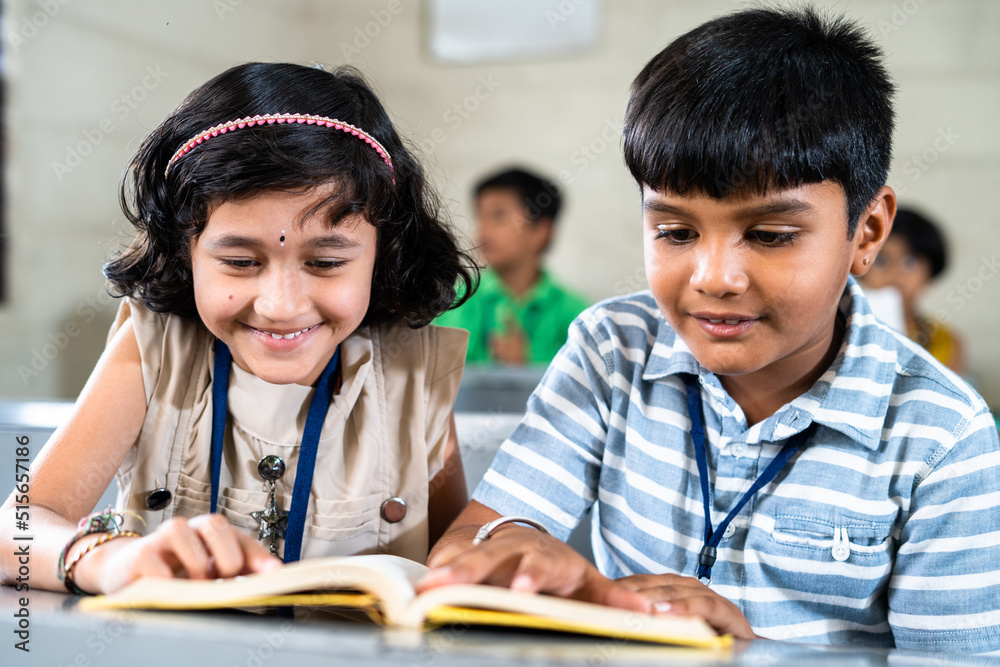 happy smiling Teenage kids studying for examination while sitting on desk at classroom by sharing book - concept of education, freindship and knowledge happy smiling Teenage kids studying for examination while sitting on desk at classroom by sharing book - concept of education, freindship and knowledge