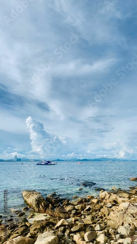 Vertical shot of a rocky coastline and the sea with several boats under the cloudy blue sky photo