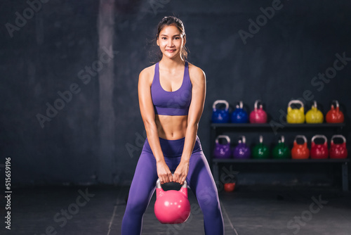 Young strong attractive Asian athletic female holding kettlebell and squat. Sporty healthy woman in purple sport wear iat the gym. photo