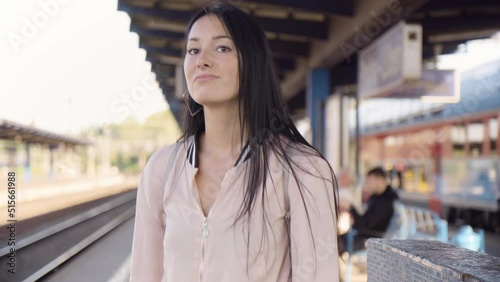 A young beautiful Caucasian woman is frustrated as she waits impatiently for a train at a train station - closeup