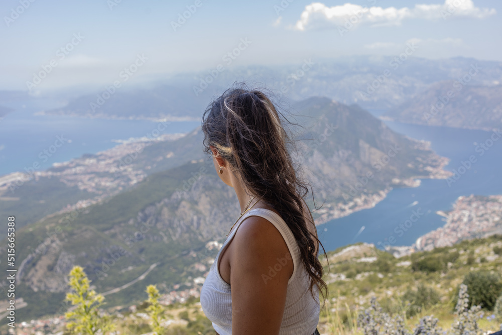 mulher no topo da montanha contemplando paisagem com mar, montanhas e céu azul.
