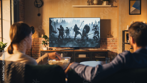 Authentic Couple Spending Time at Home, Sitting on a Couch and Watching Latest Blockbuster on Flat Screen Television Set. Man and Woman Streaming Movie or Show Using Home Cinema System.