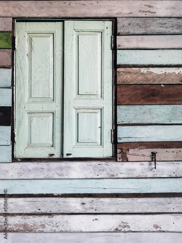 Old grunged wooden window frame painted white vintage with old colourful plywood wall. Antique window frame and old panes. Old closed window and planks of old wooden house. Background of wooden walls