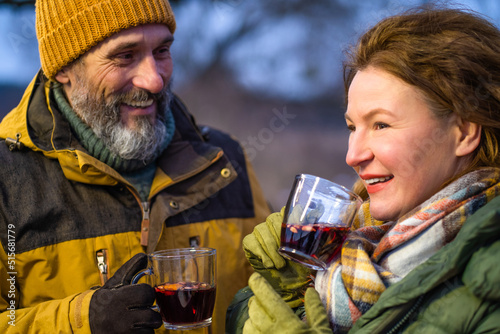 Drinking mulled wine mature couple enjoying winter romantic tour camping adventure. Romantic mature couple family outreach with hot wine near camper. Family adventure and vacation concept. 