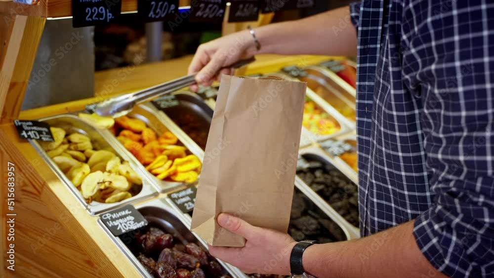man is buying healthy and sweet dried pear in grocery shop or market, taking fruit secs in paper bag