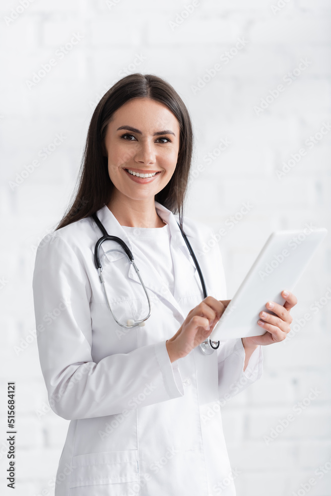 Brunette doctor smiling at camera and using digital tablet in clinic Brunette doctor smiling at camera and using digital tablet in clinic