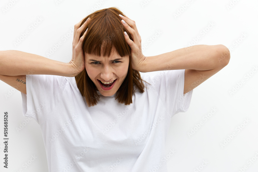 a funny, emotional woman stands on a light background in a T-shirt and holds her head with her hands while expressing emotions. Horizontal photo with an empty space for inserting an advertising layout a funny, emotional woman stands on a light background in a T-shirt and holds her head with her hands while expressing emotions. Horizontal photo with an empty space for inserting an advertising layout