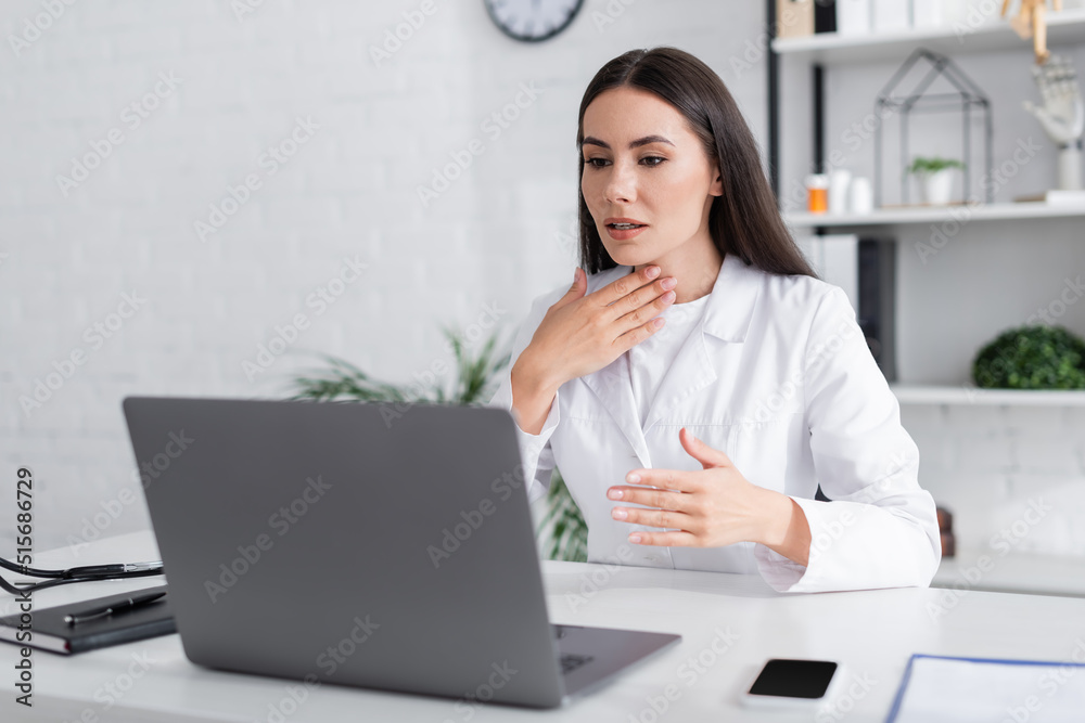 Brunette doctor having video call on laptop and touching neck in clinic Brunette doctor having video call on laptop and touching neck in clinic