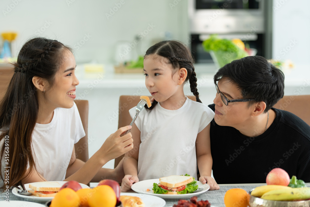 Asian father and mother Show your love to little daughter and having breakfast together happily in the dining room of the house.