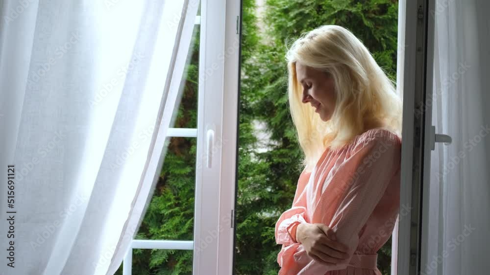 smiling blond woman at the open window to the garden smiling blond woman at the open window to the garden