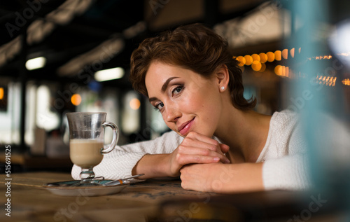 Young pensive woman in a cafe. She looks into the camera and smiles calmly. Concept of psychology and appeasement.