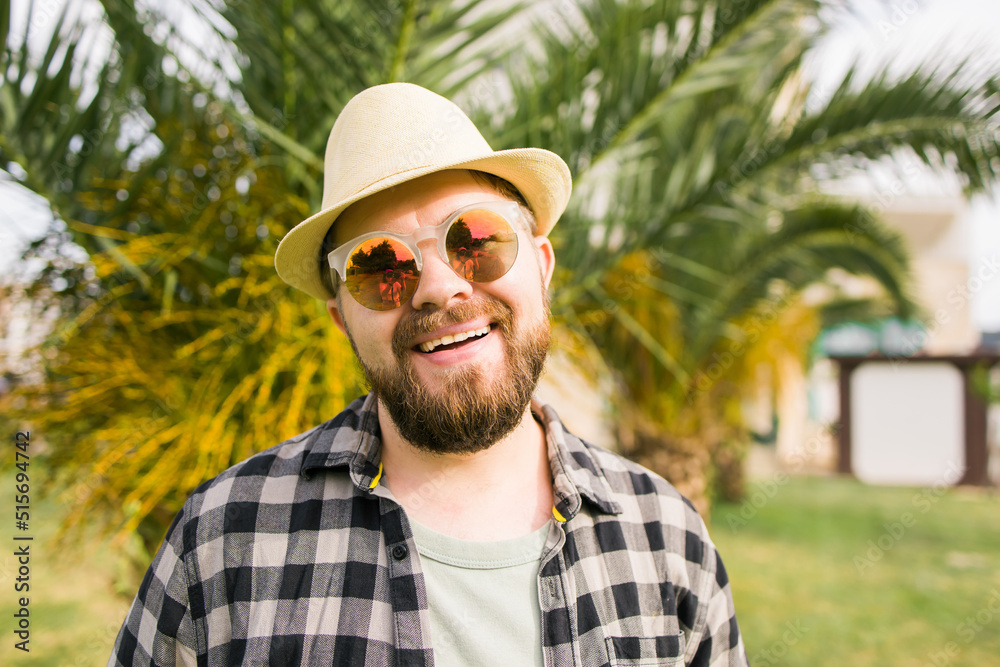 Laughing attractive man wearing hat over palm tree background - emotion and vacation travel holidays concept