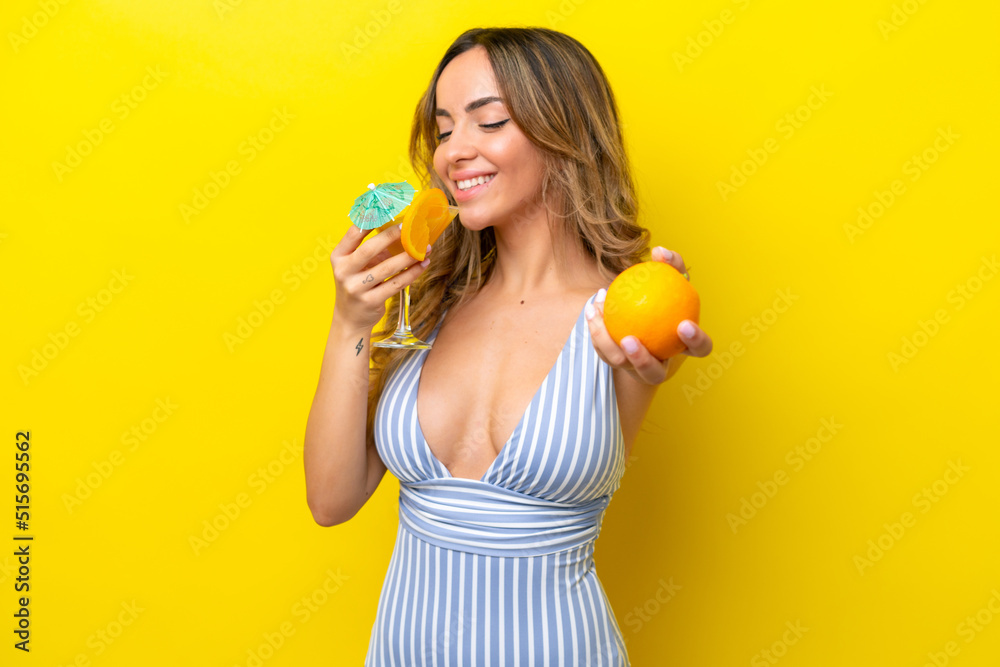 Young caucasian woman isolated on yellow background in swimsuit and holding a cocktail Young caucasian woman isolated on yellow background in swimsuit and holding a cocktail