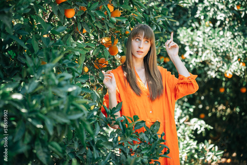 Beautiful girl in orange dress is looking up and pointing up with forefinger in orange garden