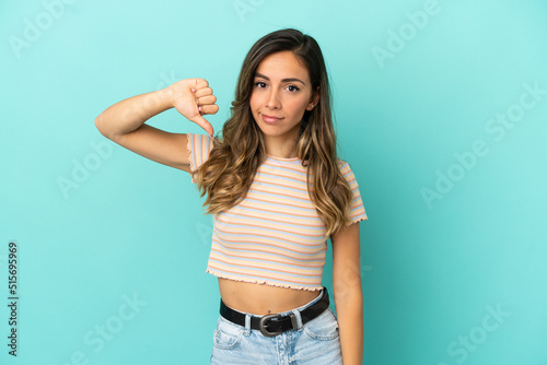 Young woman over isolated blue background showing thumb down with negative expression