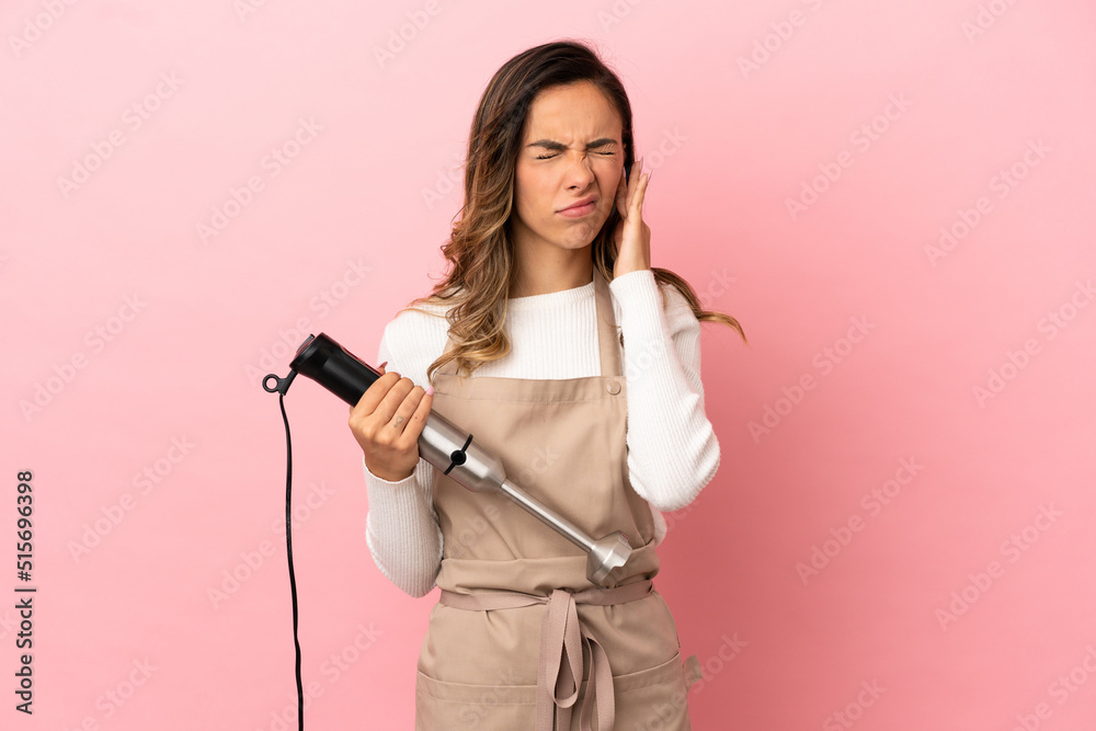 Young woman using hand blender over isolated pink background frustrated and covering ears Young woman using hand blender over isolated pink background frustrated and covering ears
