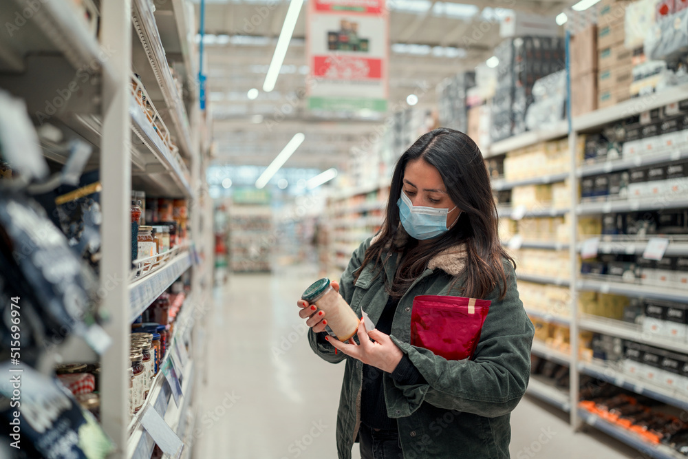 mature latin woman with mask choosing or  looking at groceries in supermarket
