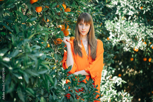 Seriously girl in orange dress is looking at camera in orange garden
