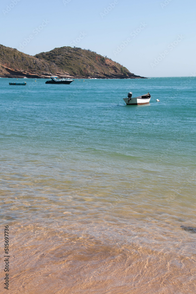 Beautiful beach of Jao Fernandez, in Buzios, Brazil, on a sunny day, surrounded by hills, blue water and red sand. 