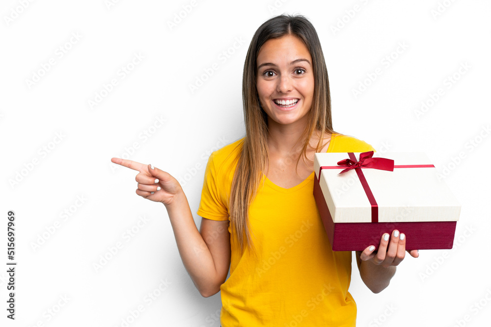 Young caucasian woman holding a gift isolated on white background surprised and pointing finger to the side Young caucasian woman holding a gift isolated on white background surprised and pointing finger to the side