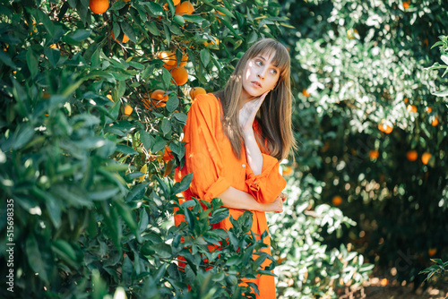 Young girl in orange dress is looking away by holding hand under chin in orange garden