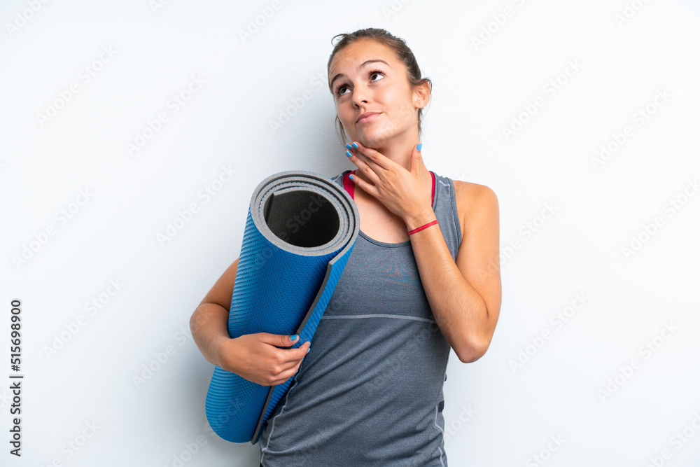 Young sport woman going to yoga classes while holding a mat isolated on white background looking up while smiling Young sport woman going to yoga classes while holding a mat isolated on white background looking up while smiling