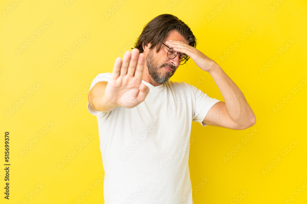 Senior dutch man isolated on yellow background making stop gesture and covering face
