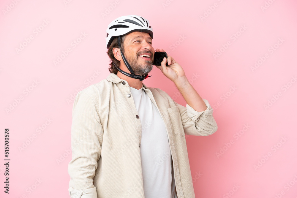 Senior dutch man with bike helmet isolated on pink background keeping a conversation with the mobile phone Senior dutch man with bike helmet isolated on pink background keeping a conversation with the mobile phone