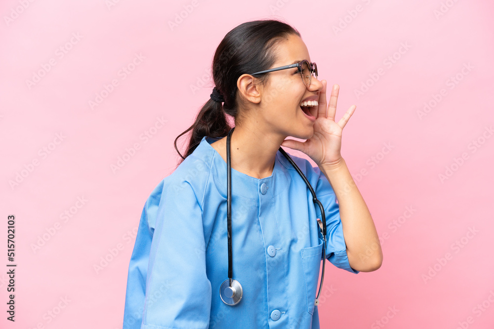 Young nurse Colombian woman isolated on pink background shouting with mouth wide open to the lateral Young nurse Colombian woman isolated on pink background shouting with mouth wide open to the lateral