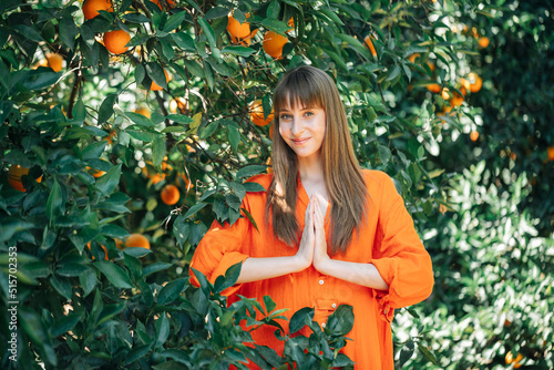 Young girl in orange dress is posing to camera by holding hands together in orange garden