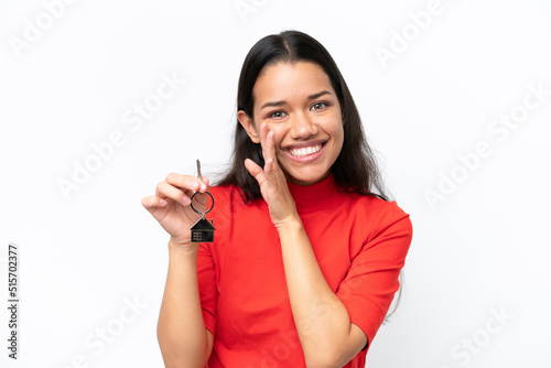 Young Colombian woman holding home keys isolated on white background whispering something