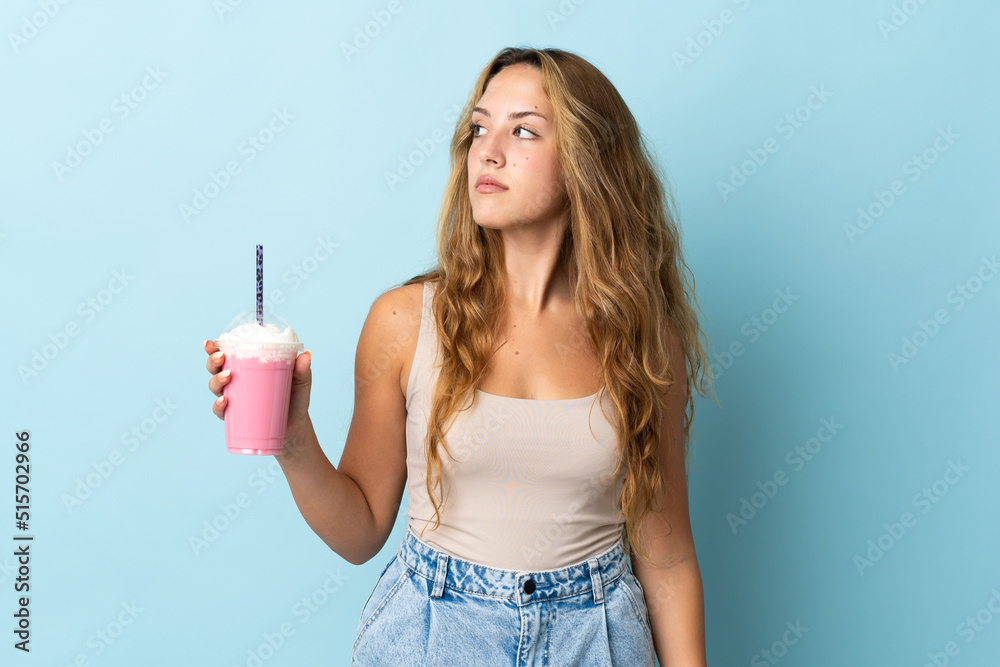Young woman with strawberry milkshake isolated on blue background looking to the side Young woman with strawberry milkshake isolated on blue background looking to the side