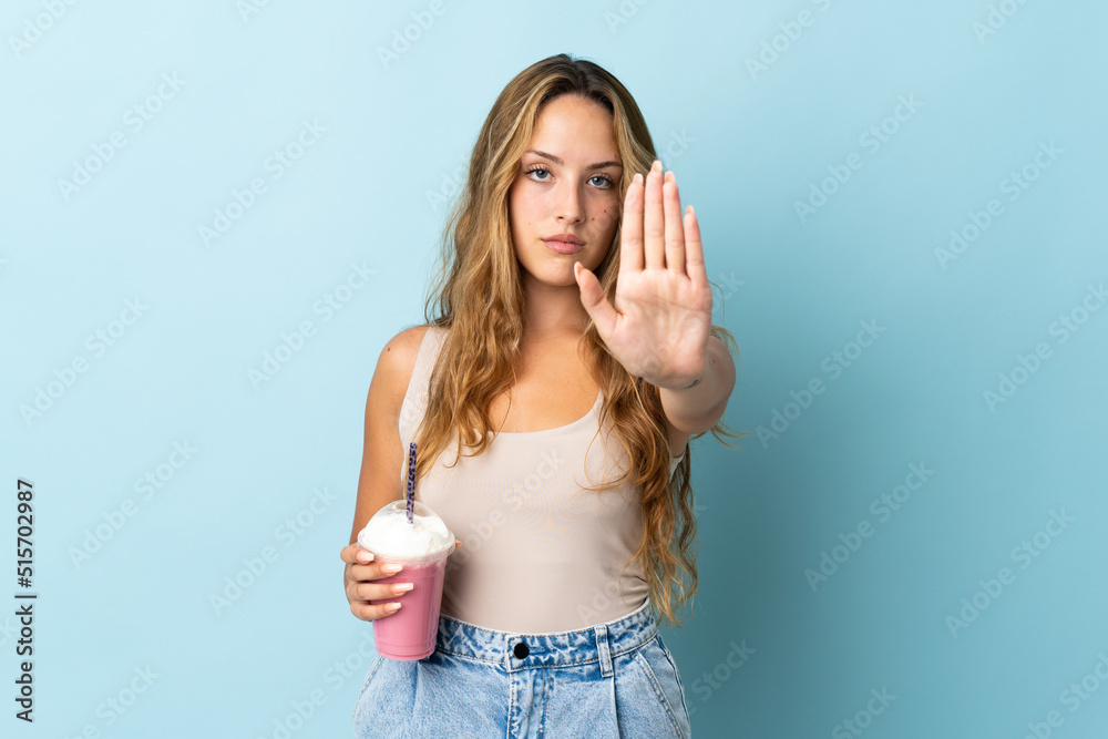 Young woman with strawberry milkshake isolated on blue background making stop gesture Young woman with strawberry milkshake isolated on blue background making stop gesture