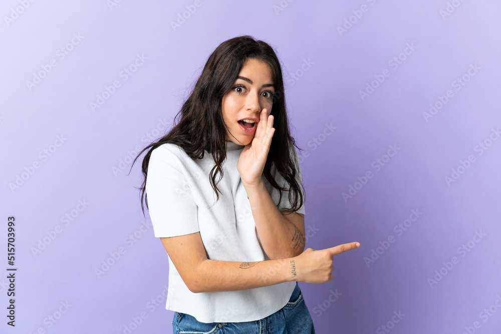 Young caucasian woman isolated on purple background pointing to the side to present a product and whispering something Young caucasian woman isolated on purple background pointing to the side to present a product and whispering something