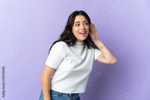 Young caucasian woman isolated on purple background listening to something by putting hand on the ear © luismolinero