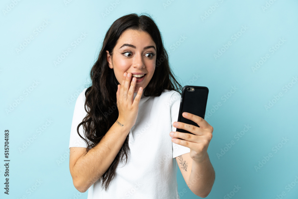 Young woman using mobile phone isolated on blue background with surprise and shocked facial expression Young woman using mobile phone isolated on blue background with surprise and shocked facial expression