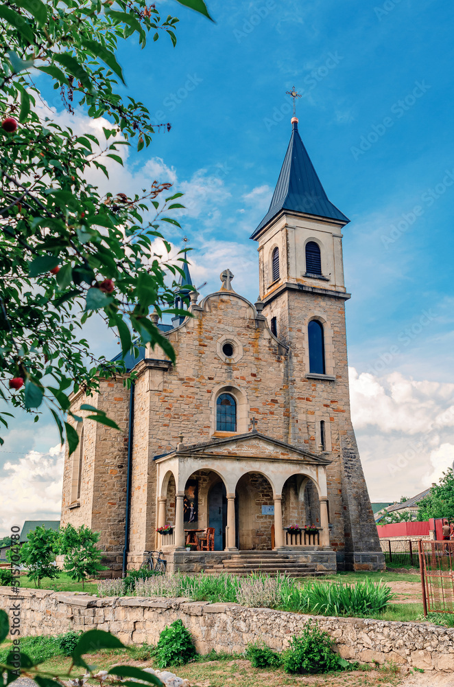 A view of the stone church through the green branches of trees. Catholicism. Religious building. A view of the stone church through the green branches of trees. Catholicism. Religious building.
