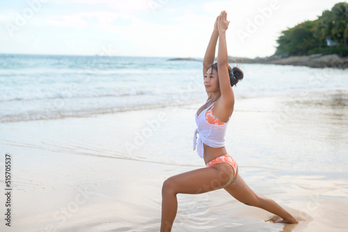 Young asian woman in bikini doing yoga on the beach, health and meditation concept