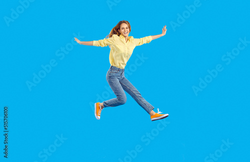Full length body size view of nice attractive lovely glad cheerful wavy-haired woman raising hands screaming laughing wearing yellow shirt jeans sneakers over blue background. People emotions concept