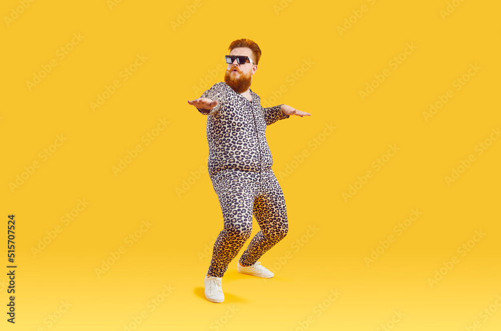 Plus size male model in funny PJs having fun in modern fashion studio. Happy carefree confident fat bearded man in comfortable leopard pajamas and cool glasses dancing isolated on yellow background - obrazy, fototapety, plakaty 