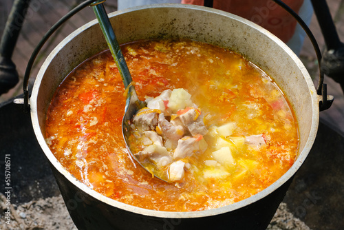 Cooking fresh-soup fish soup or uha on a fire. Cast iron cauldron with boiling fish broth. Delicious fish broth with sturgeon, and vegetables. Shallow depth of field. photo